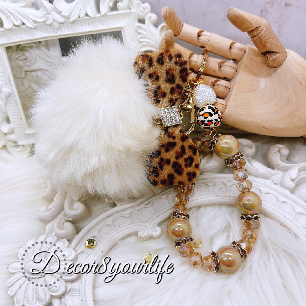 Elegant pom pom wristlet keychain featuring a large white pom pom, a faux-fur animal print bow with a rhinestone accent, acrylic beads, and rhinestone spacers. Perfect for adding a chic touch to your keys or bag, and an ideal gift for her.