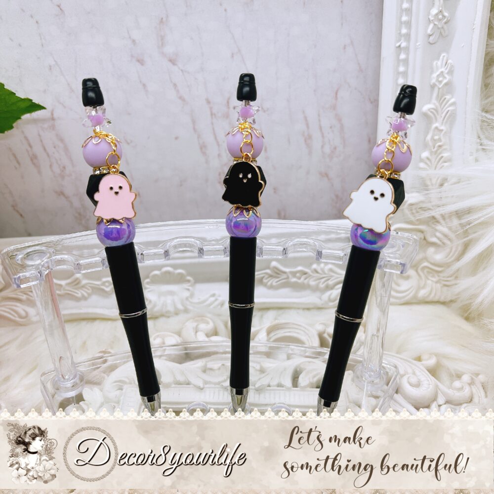 Halloween-themed beaded pen with black ink, featuring silicone and acrylic beads, rhinestone spacers, gold-tone bead caps, and an enamel ghost charm. Available in black, pink, and white ghost designs.