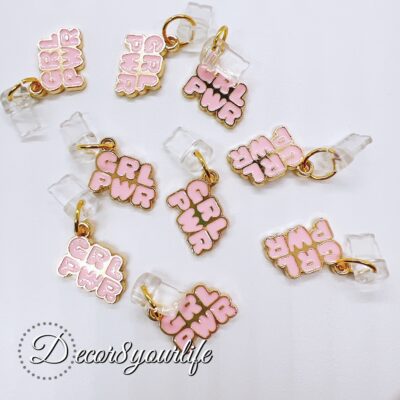 Pink 'GRL PWR' iPhone dust plug with a black strap and keychain attachment, designed to protect iPhone ports from dust and debris. The charm features a gold-trimmed, bubble-style pink lettering and is attached to a small clear bear charm. Stylish and feminine accessory for iPhone models.