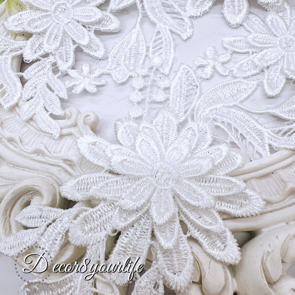 White embroidered floral appliques with detailed lace design on a decorative background