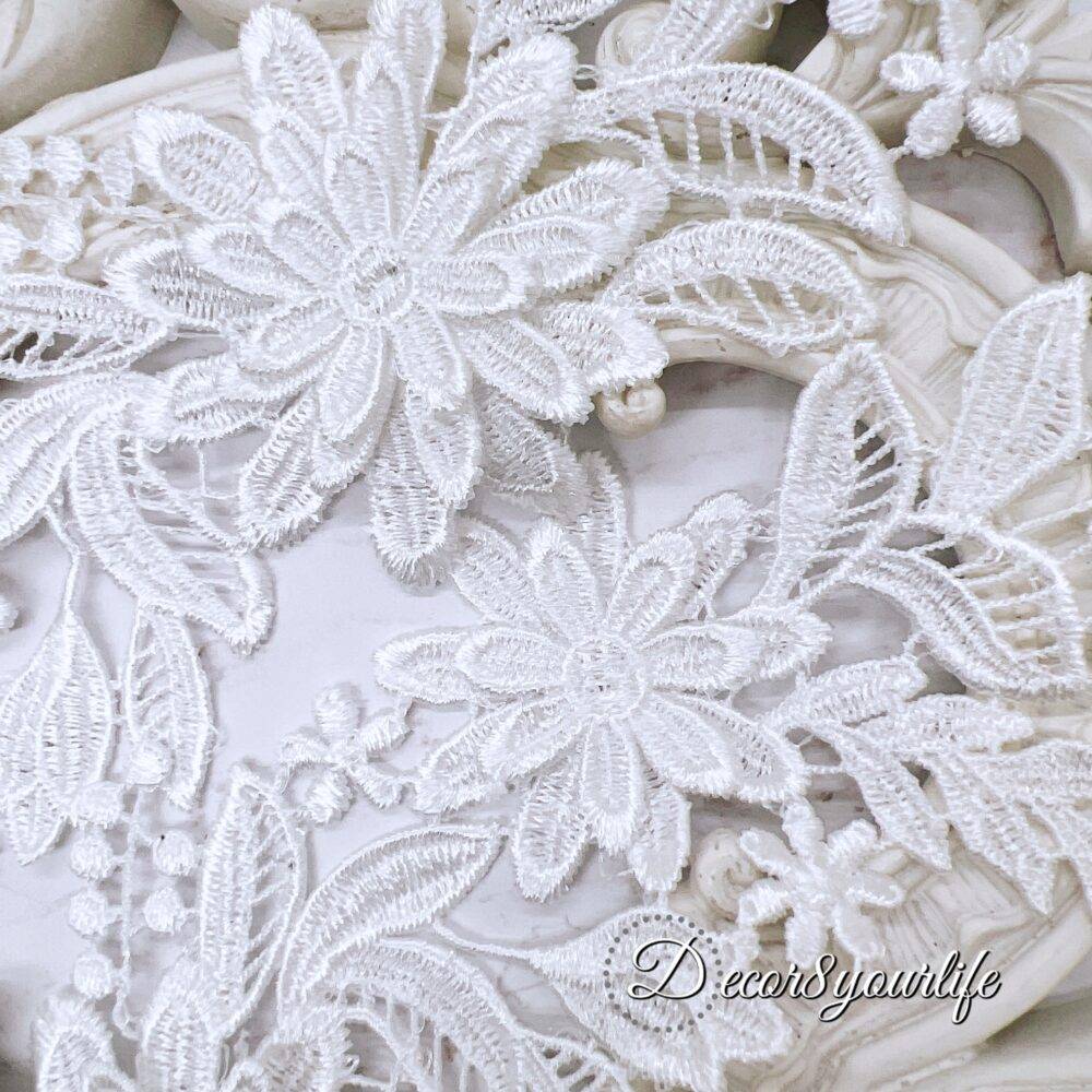 White embroidered floral appliques with detailed lace design on a decorative background