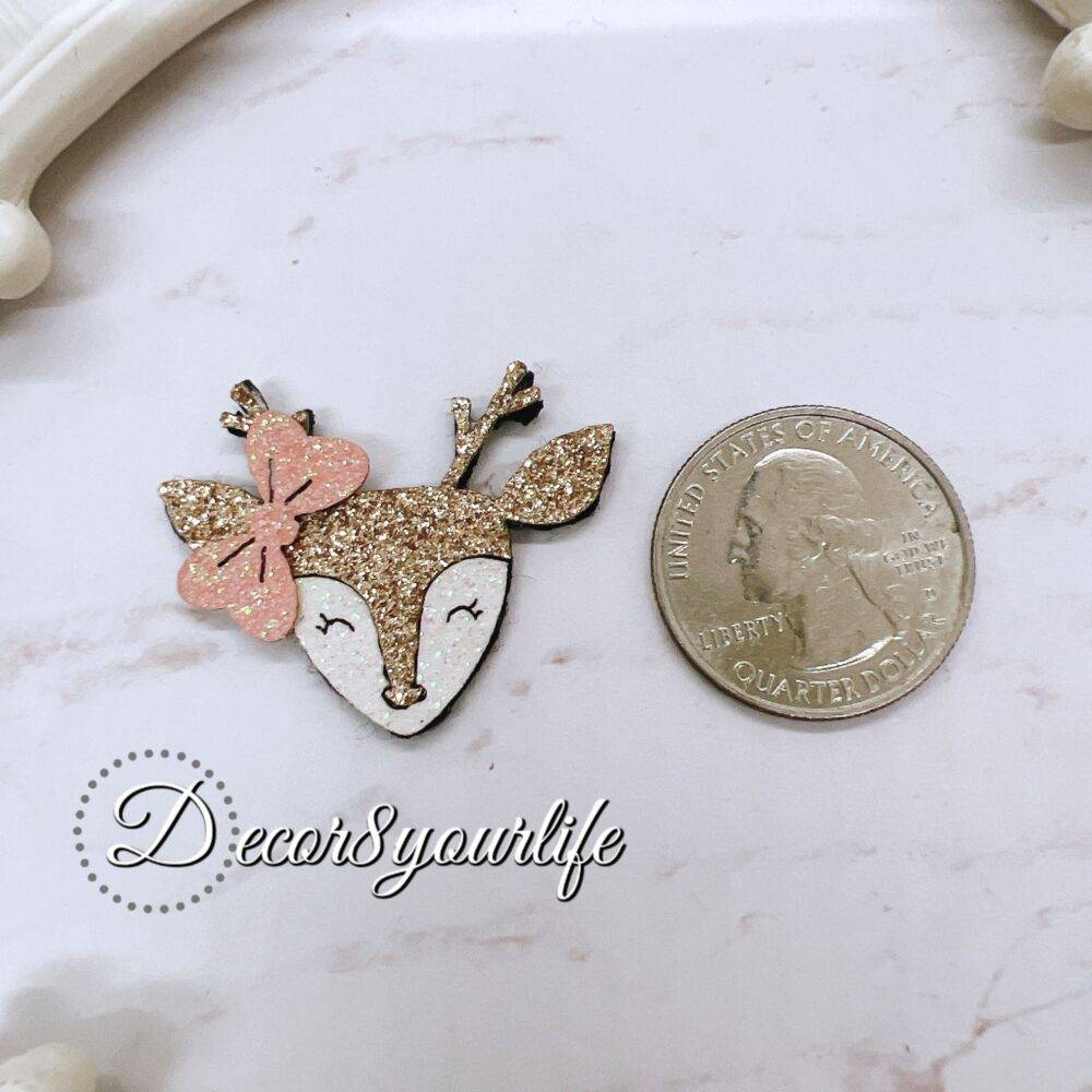 Two glittery reindeer head die-cut pieces with felt backing, featuring a pink bow on each, placed on a light-colored surface.