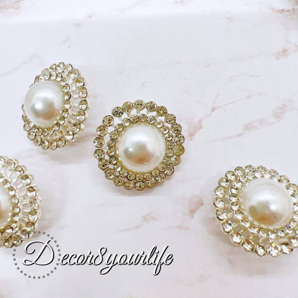 Elegant rhinestone buttons with flat-back pearl centers displayed on a shabby chic frame. Ideal for sewing and crafting projects.