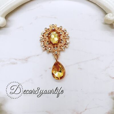 Flat-back brooch embellishment with amber gemstone and rhinestone accents, featuring a teardrop crystal and intricate gold-tone metal detailing, perfect for crafts like scrapbooks, journals, mini albums, and mixed media projects.