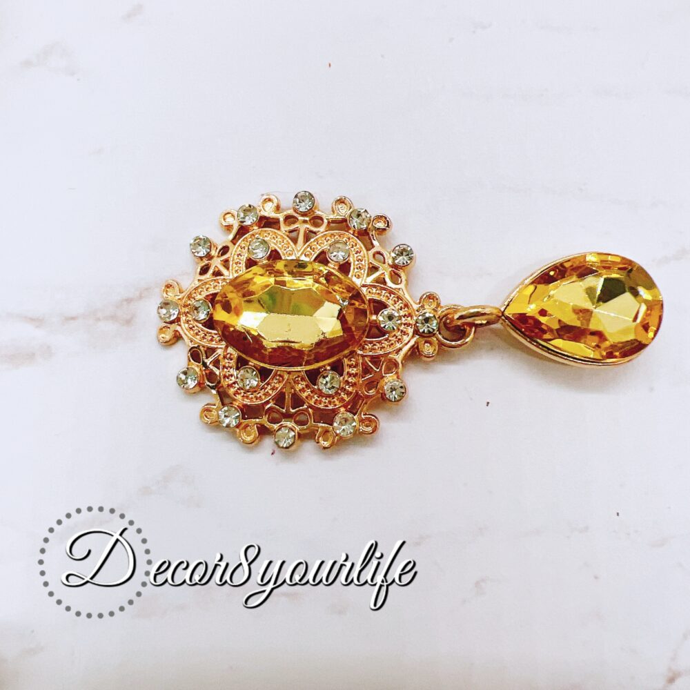 Flat-back brooch embellishment with amber gemstone and rhinestone accents, featuring a teardrop crystal and intricate gold-tone metal detailing, perfect for crafts like scrapbooks, journals, mini albums, and mixed media projects.