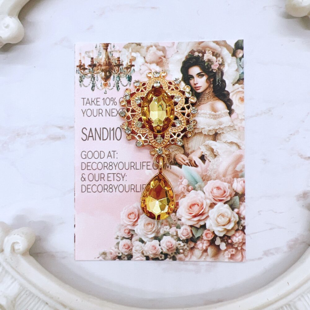 Flat-back brooch embellishment with amber gemstone and rhinestone accents, featuring a teardrop crystal and intricate gold-tone metal detailing, perfect for crafts like scrapbooks, journals, mini albums, and mixed media projects.