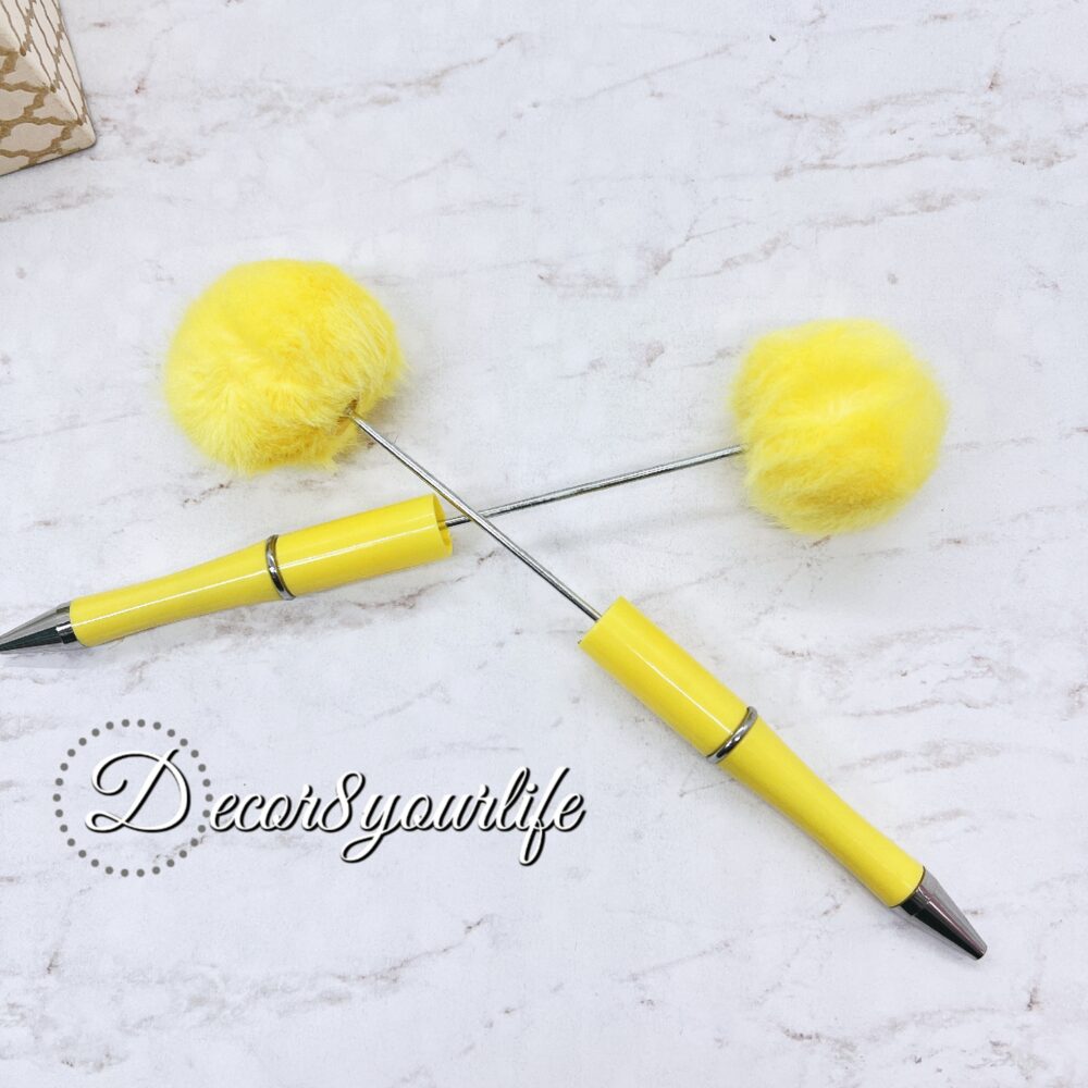 A set of two pastel pom-pom beadable pens featuring a soft, fluffy pom-pom topper and a sleek metal body.