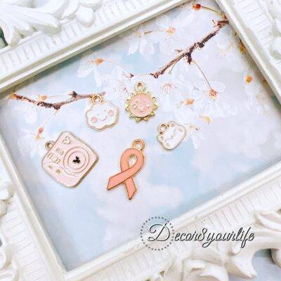 Cute pastel peach and white charm grab bag featuring assorted enamel, and metal charms in floral, heart, and camera designs—perfect for DIY jewelry and crafts.