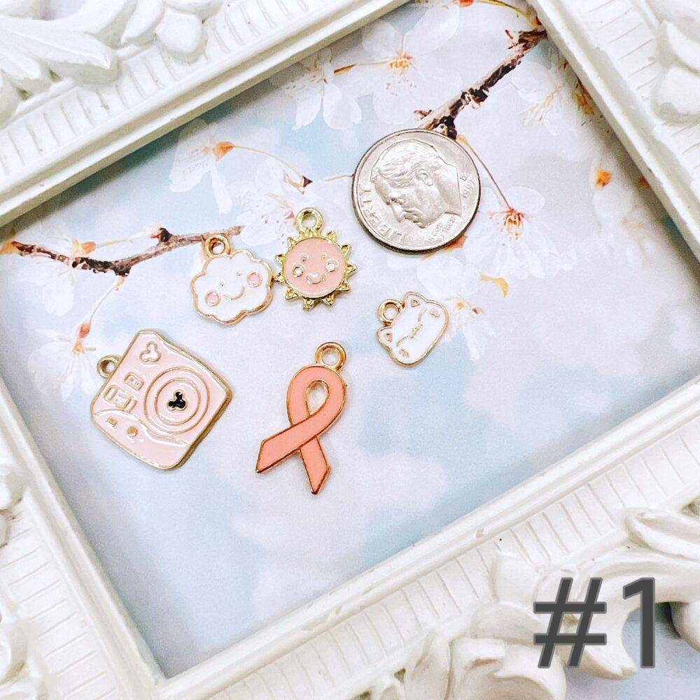 Cute pastel peach and white charm grab bag featuring assorted enamel, and metal charms in floral, heart, and camera designs—perfect for DIY jewelry and crafts.