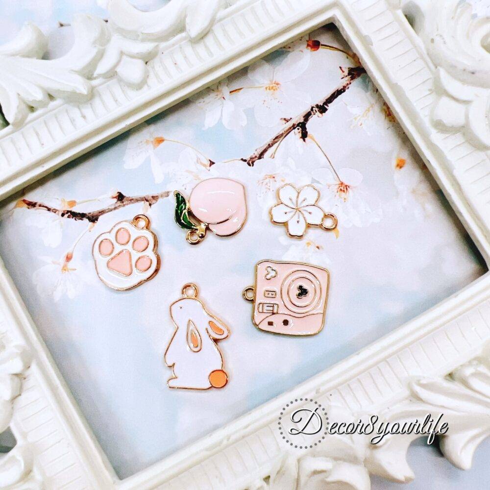 Cute pastel peach and white charm grab bag featuring assorted enamel, and metal charms in floral, heart, and camera designs—perfect for DIY jewelry and crafts.