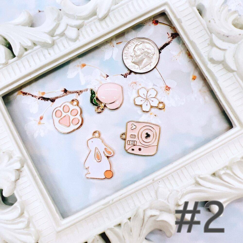 Cute pastel peach and white charm grab bag featuring assorted enamel, and metal charms in floral, heart, and camera designs—perfect for DIY jewelry and crafts.