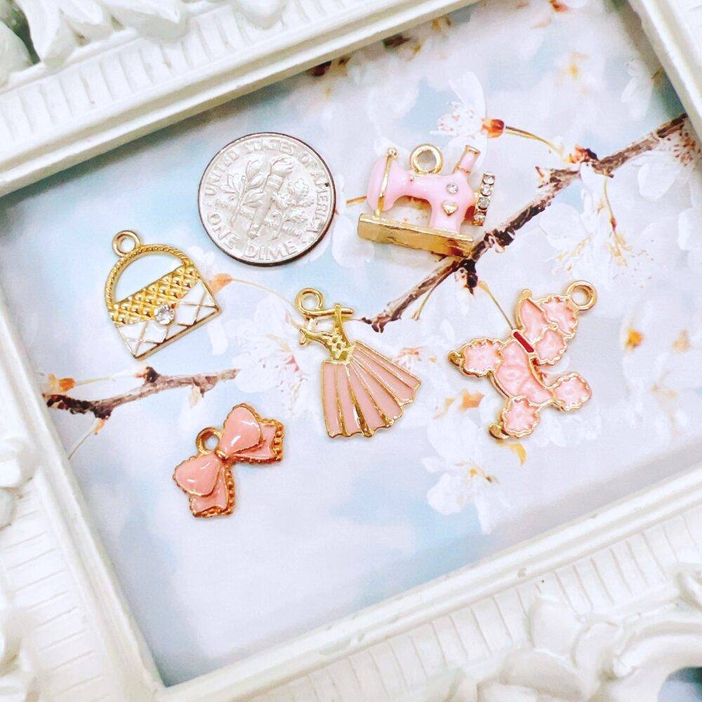 Elegant pink and white charm grab bag featuring assorted enamel, resin, and metal charms in floral, heart, and sewing-themed designs—perfect for DIY jewelry and crafts.