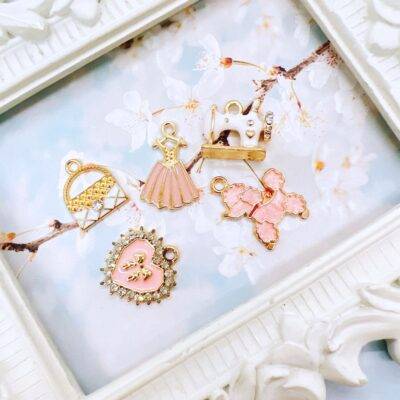 Elegant pink and white charm grab bag featuring assorted enamel, resin, and metal charms in floral, heart, and sewing-themed designs—perfect for DIY jewelry and crafts.