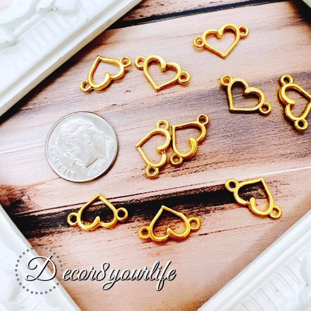 A set of gold-tone heart pendant connectors displayed on a wooden surface with a U.S. dime for size reference.