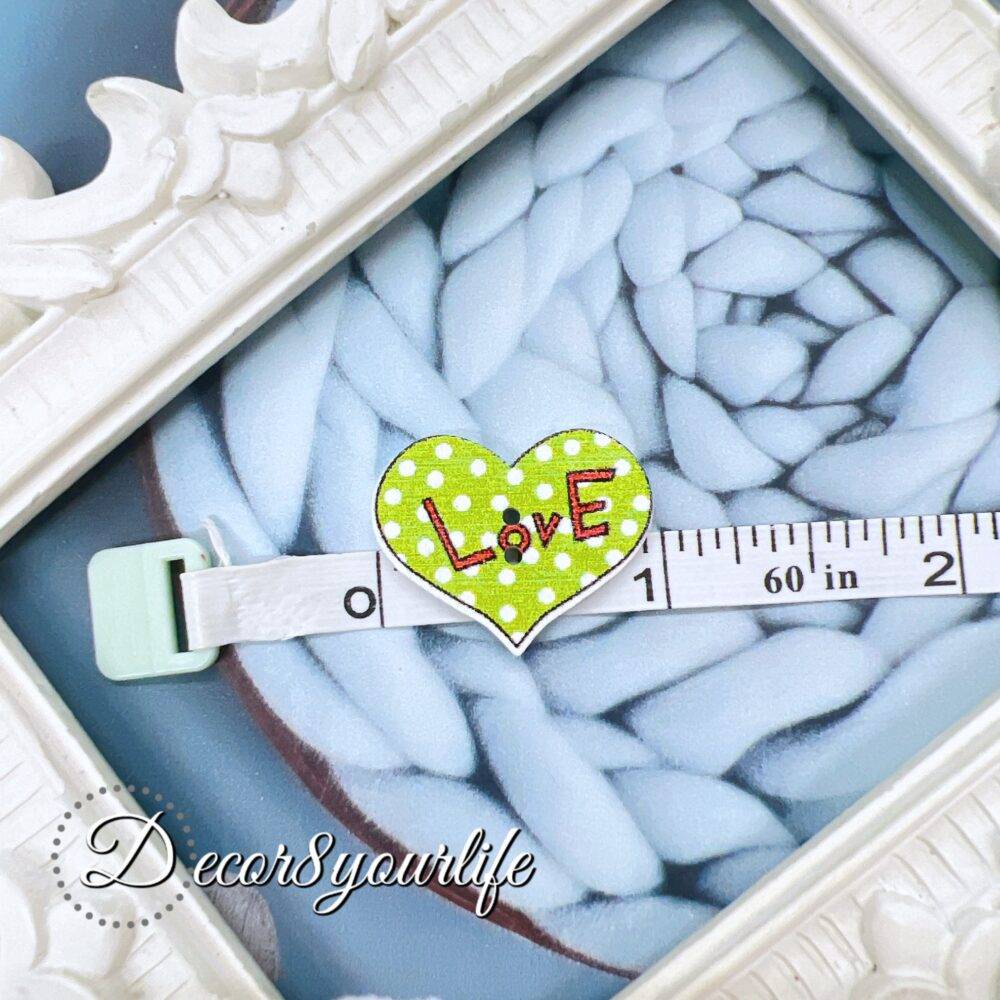 A set of ten heart-shaped wooden buttons with a pink "LOVE" design, displayed inside a white ornate frame. These 1-inch buttons are perfect for card-making, scrapbooking, journaling, and mixed media projects.