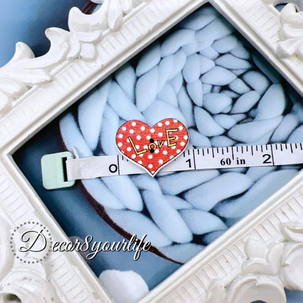 A set of ten heart-shaped wooden buttons with a pink "LOVE" design, displayed inside a white ornate frame. These 1-inch buttons are perfect for card-making, scrapbooking, journaling, and mixed media projects.