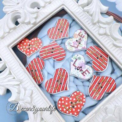 A set of ten heart-shaped wooden buttons with a pink "LOVE" design, displayed inside a white ornate frame. These 1-inch buttons are perfect for card-making, scrapbooking, journaling, and mixed media projects.