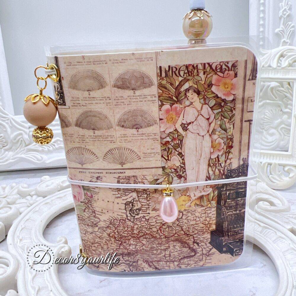 There’s something magical about putting pen to paper, and this shabby chic traveler's notebook makes it even more special! Handcrafted with love, it features two altered mini composition notebooks, a handy pocket for essentials, and the cutest beaded pen to match.