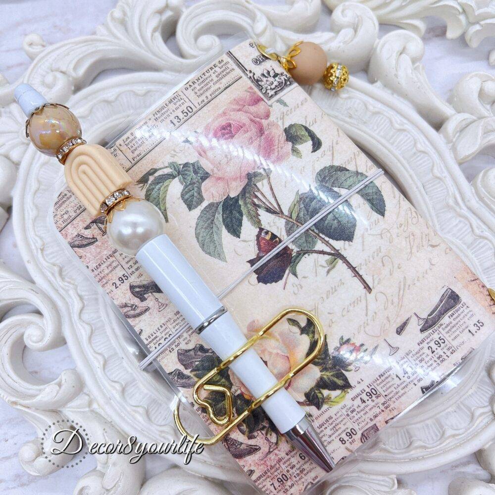 There’s something magical about putting pen to paper, and this shabby chic traveler's notebook makes it even more special! Handcrafted with love, it features two altered mini composition notebooks, a handy pocket for essentials, and the cutest beaded pen to match.