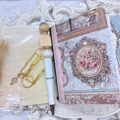 There’s something magical about putting pen to paper, and this shabby chic traveler's notebook makes it even more special! Handcrafted with love, it features two altered mini composition notebooks, a handy pocket for essentials, and the cutest beaded pen to match.