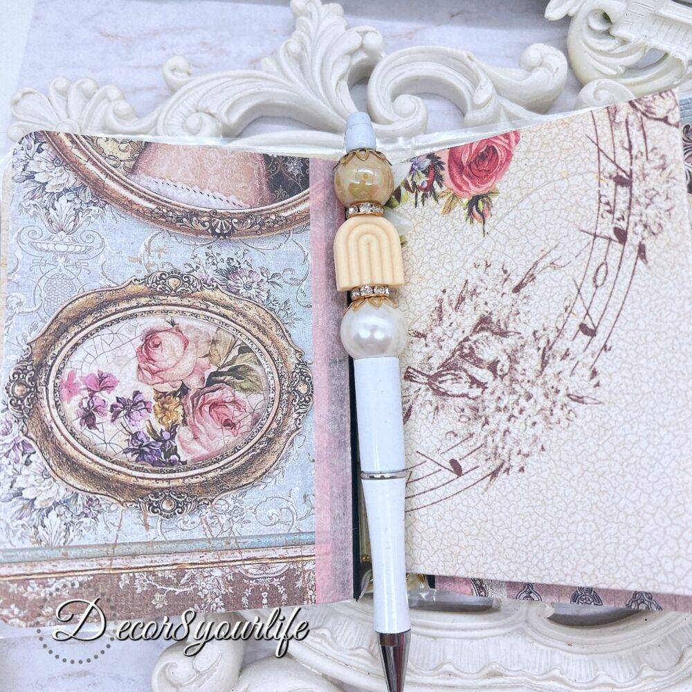 There’s something magical about putting pen to paper, and this shabby chic traveler's notebook makes it even more special! Handcrafted with love, it features two altered mini composition notebooks, a handy pocket for essentials, and the cutest beaded pen to match.