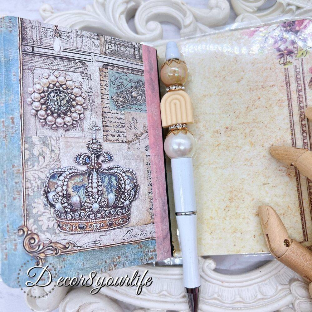 There’s something magical about putting pen to paper, and this shabby chic traveler's notebook makes it even more special! Handcrafted with love, it features two altered mini composition notebooks, a handy pocket for essentials, and the cutest beaded pen to match.