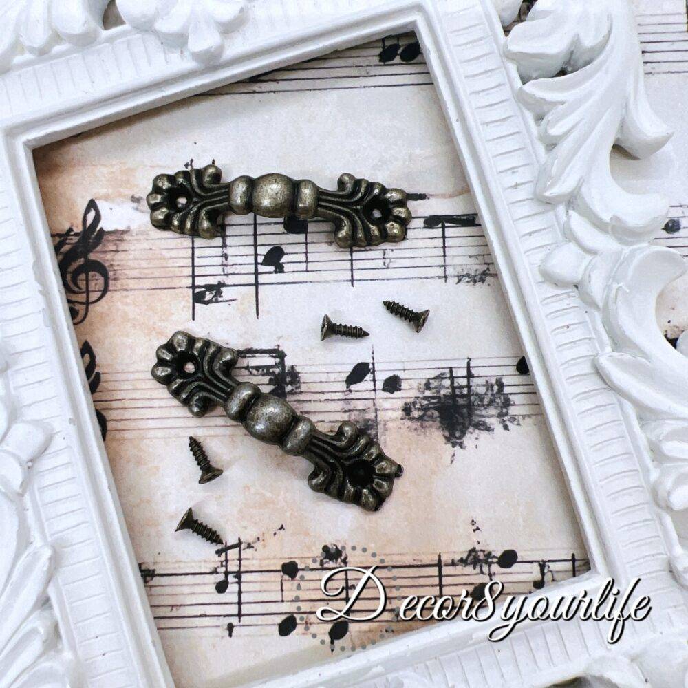 set of two vintage-style drawer handles with an antique bronze finish, displayed on a decorative sheet of music paper within a white ornate frame. Small matching screws are included for easy attachment, making them perfect for DIY furniture restoration, mini album projects, or decorative crafts.