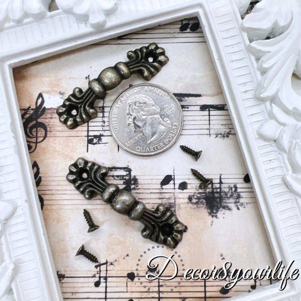 set of two vintage-style drawer handles with an antique bronze finish, displayed on a decorative sheet of music paper within a white ornate frame. Small matching screws are included for easy attachment, making them perfect for DIY furniture restoration, mini album projects, or decorative crafts.