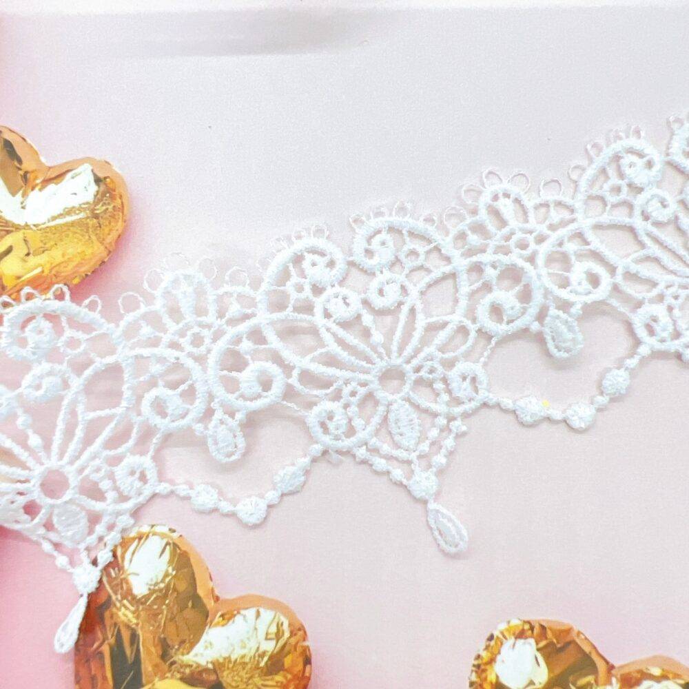 Delicate white embroidered lace trim with floral patterns, gently draped across a wooden mannequin hand on a soft, neutral background—ideal for shabby chic crafts, bridal embellishments, junk journals, and handmade cards