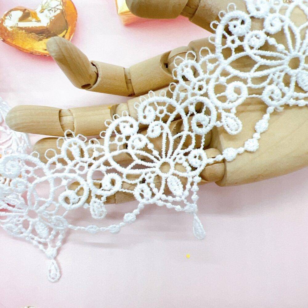Delicate white embroidered lace trim with floral patterns, gently draped across a wooden mannequin hand on a soft, neutral background—ideal for shabby chic crafts, bridal embellishments, junk journals, and handmade cards