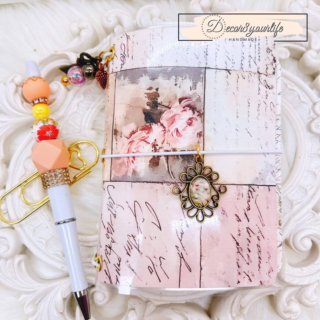 Handmade vintage-style traveler's notebook with laminated cover, pink and neutral diamond pattern, hanging charms, and coordinating beaded pen