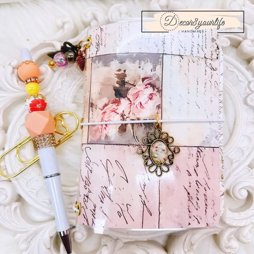 Handmade vintage-style traveler's notebook with laminated cover, pink and neutral diamond pattern, hanging charms, and coordinating beaded pen