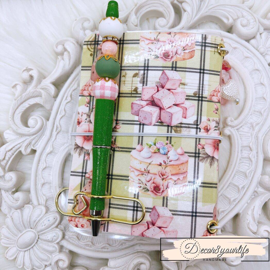 Pocket size laminated traveler’s notebook with Bunny Bakes & Pantry Tales dessert design, chunky charms, handmade beaded pen, and gold-tone paperclip pen holder.
