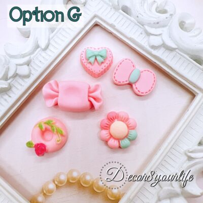 Close-up photo of assorted pink flat-back cabochons. The cabochons include bow shapes, candy shapes, and character accents. These resin embellishments are sold in a 5-pack and can be glued to planner dashboards, mini albums, hair bows, shaker key-chains, and gift tags.