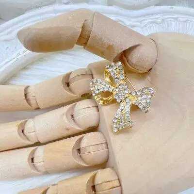 Gold rhinestone bow brooch with clear crystals in a gold setting. Vintage style gold bow brooch with sparkling rhinestones used as a journal embellishment. Elegant rhinestone bow pin for crafts, scrapbooking, and shabby chic decor.