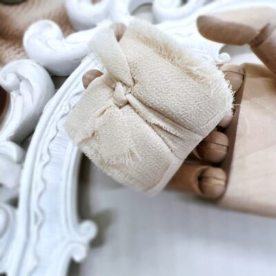 Beige chiffon sheer ribbon with soft frayed edges rolled on a spool for journaling, gift wrapping, and vintage craft projects.