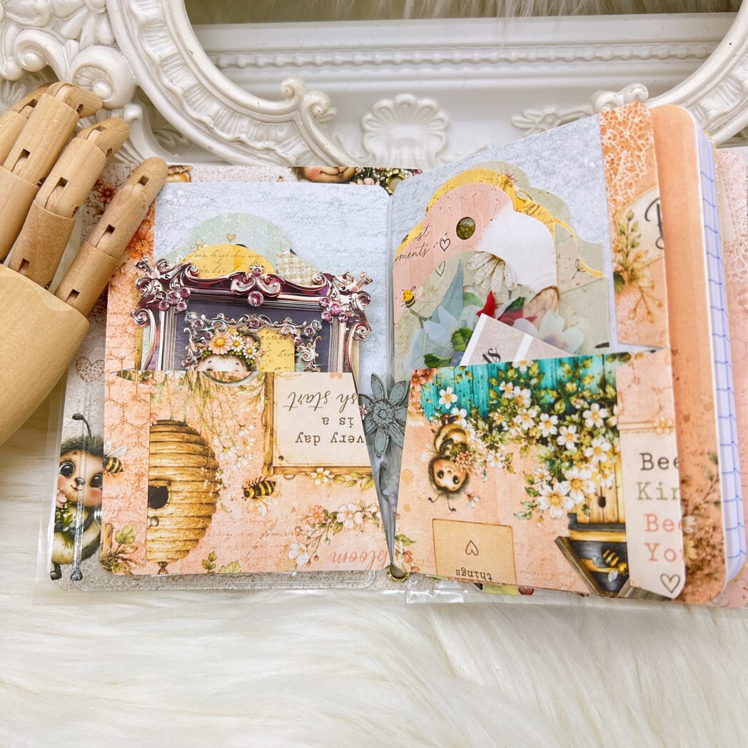 Coordinating accessories included with the Honey Bees & Summer Breeze traveler's notebook, including a handmade beaded pen, decorative bookmarks, oversized gold paper clips, and dimensional embellishments.