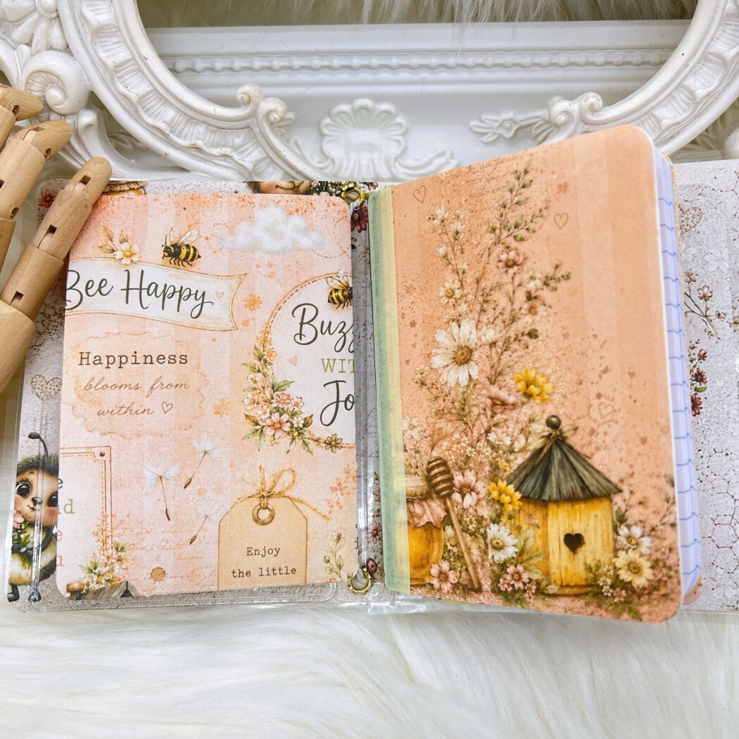 Open Honey Bees & Summer Breeze handmade micro traveler's notebook showing two altered mini composition notebooks, transparent storage pocket, handmade folders, bookmarks, and coordinating bee-themed papers.