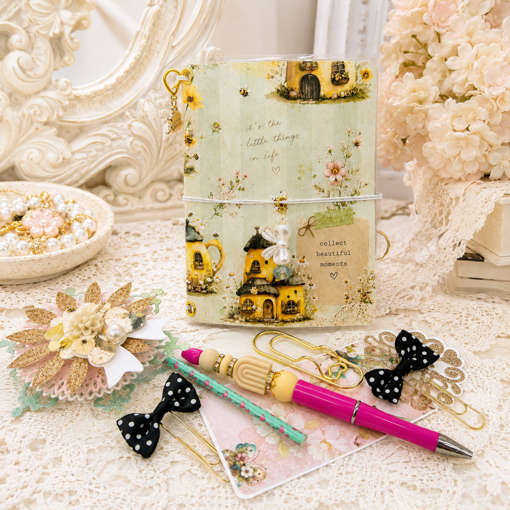 Coordinating accessories included with the Honey Bees & Summer Breeze traveler's notebook, including a handmade beaded pen, decorative bookmarks, oversized gold paper clips, and dimensional embellishments.