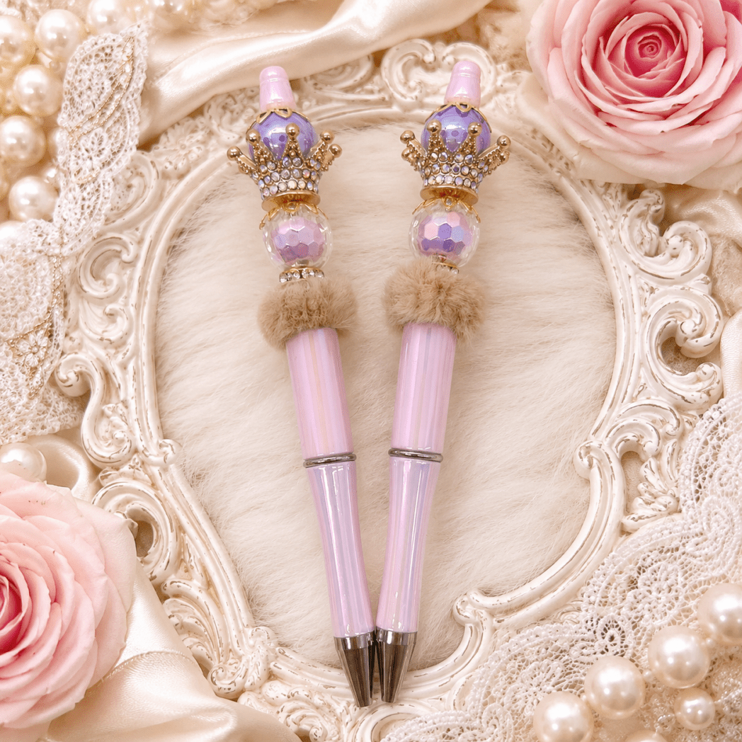 Luxury handmade beaded pens by Decor8yourlife featuring jeweled crown toppers, blush pink crystal beads, pearl accents, and elegant feminine stationery displayed on a vintage ivory frame.