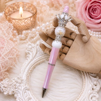 Handmade Luxury Pearl Crown Pen featuring a premium pastel pink iridescent polymer barrel, luminous iridescent pearl focal bead, jeweled silver crown topper, elegant silver accents, and refillable black ink.