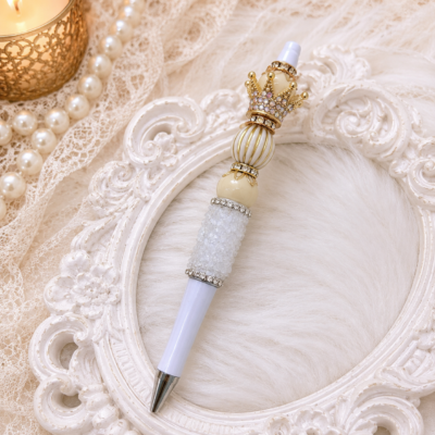 This handmade Luxury Beaded Crown Pen features creamy pearl-inspired beads, a shimmering White Rock Candy accent bead that catches the light beautifully, sparkling rhinestone spacers, and a jeweled crown topper, creating a timeless writing accessory that feels both elegant and unique.